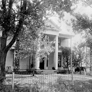 Close-up of multistory house with covered porch and balcony under trees inside fence