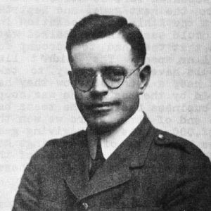 White man smiling short combed hair round glasses in suit and tie