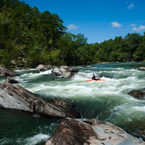 man in kayak navigating white water rapids with paddle