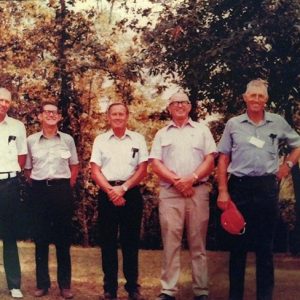 Five white men standing together with autumn trees behind them
