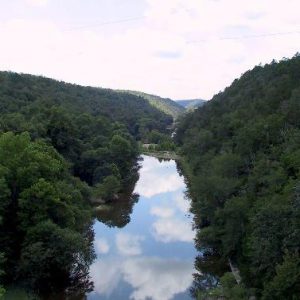 Clouds and trees reflected in river with mountains in the distance