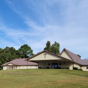 Single story tan church building with brown roof and covered entrances