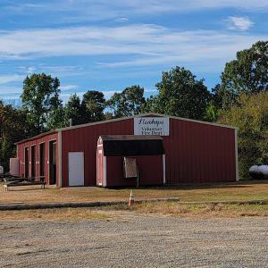 Single story red metal building with four bay doors and trees in background