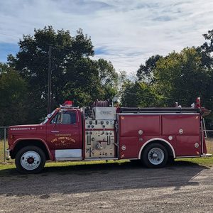 Red fire department vehicles parked on gravel road with trees in background